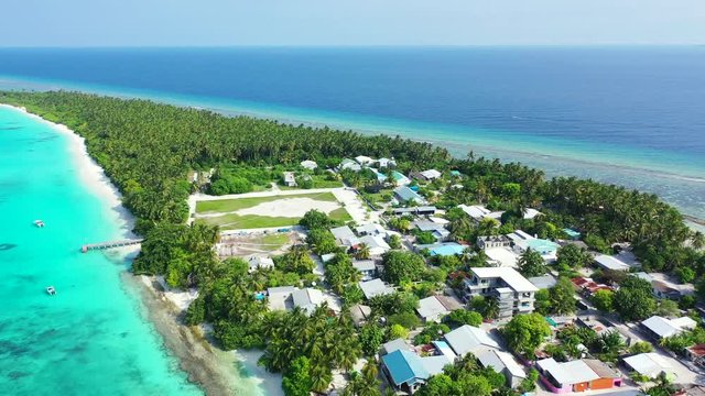 Aerial view flying over a thin tropical island with a village on it and a forest in the background. Surrounded by the turquoise sea of the Gulf of Thailand. Looking down, diagonal flight.