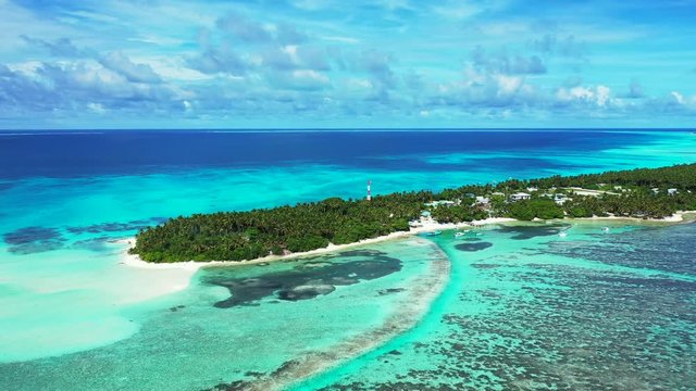 Aerial view of a the turquoise sea in Thailand, a tropical island with a village on it. Reefs in the water.  Blue water in the background under  a blue sky