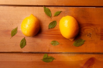 Two yellow lemons and leaves are laying on a wooden surface