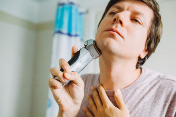 Young man shaving his face using an electric razor  in the bathroom