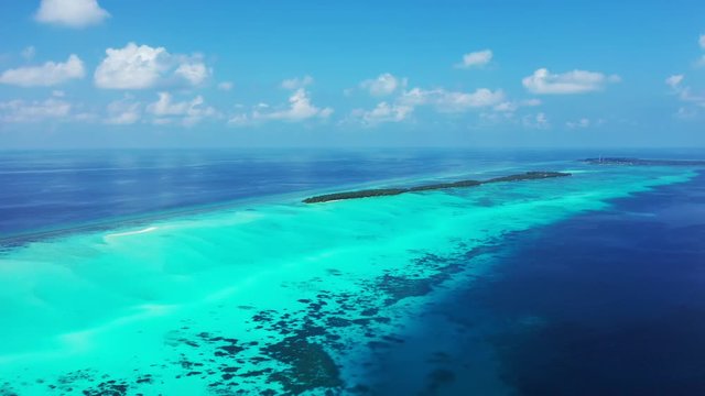 Aerial view of a strip o turquoise water surrounded by blue water. With islands and reefs in the water. An island in the distance, Bali, blue sky with clouds.