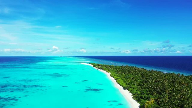 Aerial view along a tropical island with some trees on it. In turquoise water in Bali under a blue sky. static