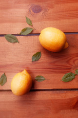 Two yellow lemons and leaves are laying on a wooden surface