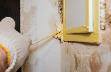 Worker is filling spray foam near electrical panel. Maintenance repair works renovation in the flat. Restoration indoors.