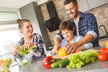 Family at home standing in kitchen together father teaching son cutting vegetables cheerful