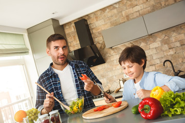 Family at home standing in kitchen together father trying tomato cutted by boy smiling cheerful
