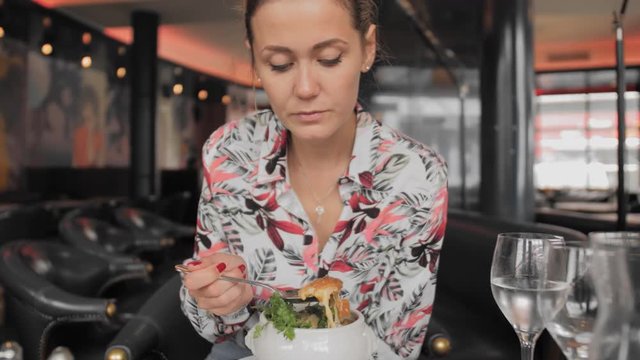 Beautiful female tourist in a colorful shirt spoon eats traditional French onion soup with croutons, melted cheese and herbs in a Paris restaurant. Slow Motion.
