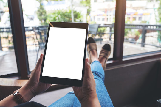 Mockup image of a woman holding black tablet pc with blank white screen while sitting and relaxing in cafe
