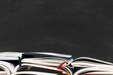 Knowledge concept. Stacked open books over blur empty black chalkboard. Copy space.