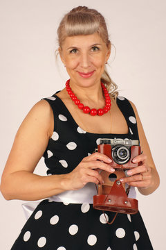Beautiful blond woman in pinup style, dressed in a polka-dot dress holding a camera in front of her, white background