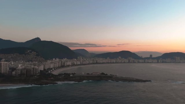 Incredible sunrise over the Copacabana fort with in the background the Corcovado mountain panning towards the sun with the Sugarloaf mountain in Rio de Janeiro