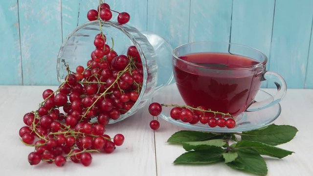 The cup of the hot redcurrant tea stands on the white table next to ripe red currant on a pale blue background 