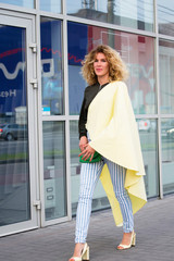 stylish curly-haired girl walks in the city near a glass shop window