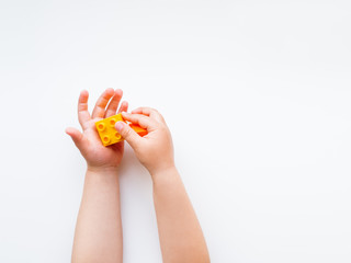 Child is playing with colorful constructor blocks. Kid's hands with bricks toy on white background. Educational toy, flat lay, top view.