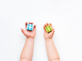 Fototapeta na wymiar Child is playing with colorful constructor blocks. Kid's hands with bricks toy on white background. Educational toy, flat lay, top view.
