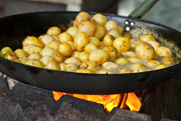 Roast potatoes in a large pan. Delicious food at the festival. Field kitchen at the hearth. Young round potatoes are fried in oil.