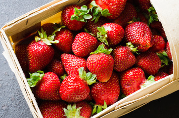 Fresh ripe strawberries in a wooden basket on a dark background. Organic juicy berries.