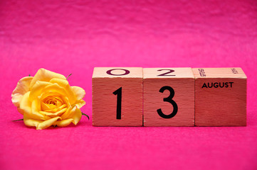 13 August on wooden blocks with a yellow rose on a pink background