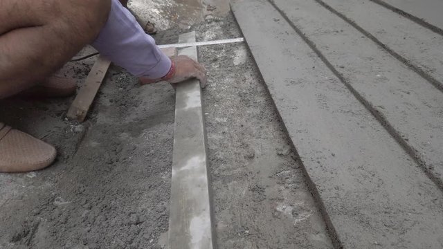 Indian mason working on a cement pathway with parallel lines on the side of the road street. 4k slow motion stabilized gimbal handheld close-up