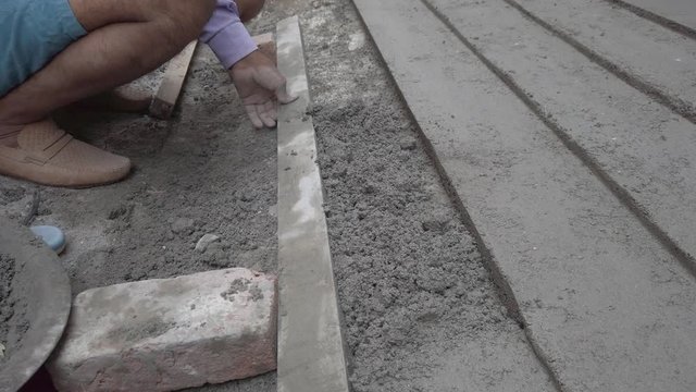 Indian mason working on a cement pathway with parallel lines on the side of the road street. 4k slow motion stabilized gimbal handheld close-up