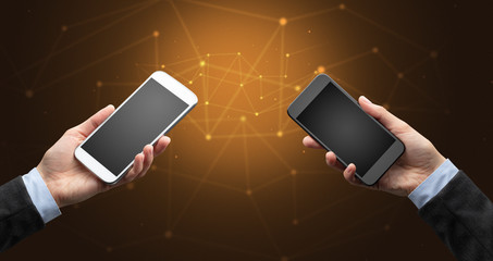 Close up of two hands holding smartphones to each other, wireless connection concept