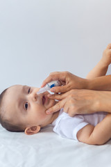 Fototapeta premium Little boy getting nasal drops. Pediatrician putting saline drops in infant's nose. Mother hands clearing the nose of baby. 6-month baby boy gets nose drops.
