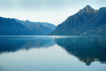Fisherman in traditional conoe swimming on lake at the morning scenery with light fog and mountain landscape.