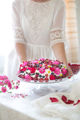 White isolated background with clipping paths homemade Berry Fruit cake, homemade biscuit cake with cream, in woman hands against of light summer flowers background