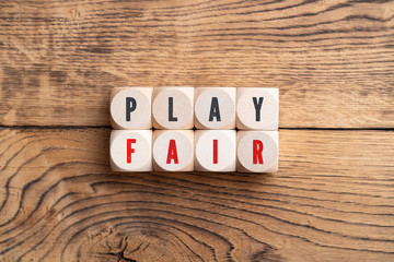 PLAY FAIR spelled with red and black letters on eight small wood blocks over rustic wooden...