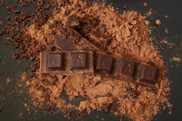 Chocolate bars with word CACAO and cacao powder on black table 