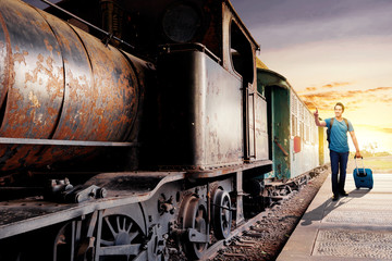 Asian man with suitcase bag and backpack standing and pointing a steam locomotive on station