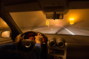 View from car on foggy road on highway at night. Hands on the wheel.