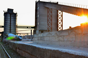 Concrete mixer truck at an industrial plant producing cement or concrete against a sunset and sun...