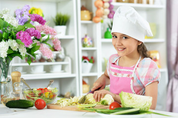 Cute girl preparing delicious fresh salad in kitchen