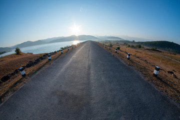 Sunrise at the reservoir, clear blue sky, wide angle from Lens Fisheye, straight road ahead over the dam,March 9, 2019, Khlong Din Daeng Reservoir, Nakhon Si Thammarat, Thailand