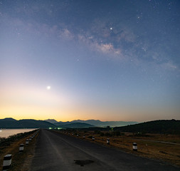 Twilight morning light Before sunrise At the reservoir, straight road ahead over the dam, the Milky Way in the early morning