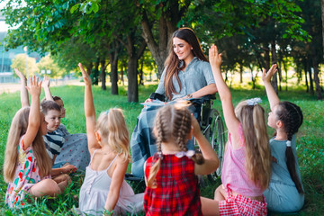 Disabled teacher conducts a lesson with children in nature. Interaction of a teacher in a wheelchair with students.