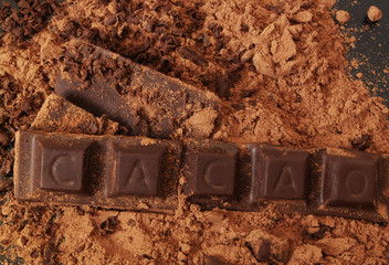Chocolate bars with word CACAO and cacao powder on black table 