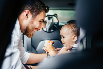 Smiling father putting baby in child seat, fastening seatbelt - Family transportation, lifestyle concept - Powered by Adobe