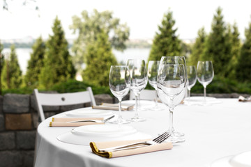 Wedding table setting decorated with fresh flowers in a brass vase. Wedding floristry. Banquet table for guests outdoors with a view of green nature. Bouquet with roses, eustoma and eucalyptus leaves