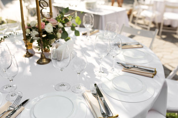 Wedding table setting decorated with fresh flowers in a brass vase. Wedding floristry. Banquet table for guests outdoors with a view of green nature. Bouquet with roses, eustoma and eucalyptus leaves