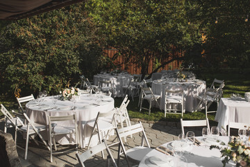 Wedding table setting decorated with fresh flowers in a brass vase. Wedding floristry. Banquet table for guests outdoors with a view of green nature. Bouquet with roses, eustoma and eucalyptus leaves