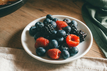 Forest berries: raspberries, blueberries, on a plate. Breakfast table setting. Morning lifestyle concept.