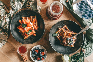 Belgian waffles with berries, ice cream and chocolate. Breakfast table setting. Morning lifestyle...