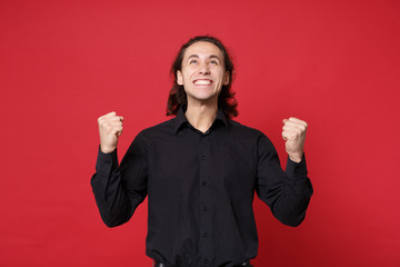 Handsome stylish young curly long haired man in black shirt posing isolated on red wall background...