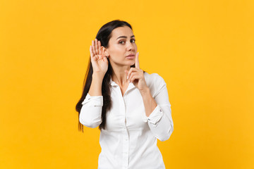 Portrait of curious young woman in white shirt saying hush be quiet with finger on lips shhh...