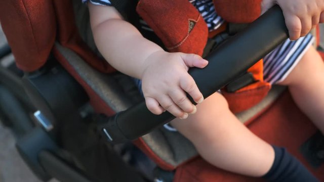 A child rides in a baby carriage, putting his hand on the handle