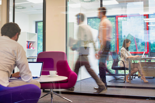 A Working Office With People Walking Out Of Focus, Concept Of A Real Life Busy Office Environment