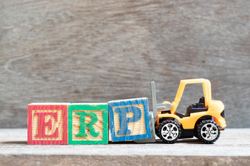 Toy forklift hold letter block P to complete word ERP (Abbreviation of Enterprise Resource Planning)  on wood background