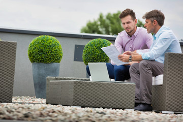 Two attractive business man sitting outdoors and discussing work whilst looking at laptop, they are casually dressed and culd be in a new start up business